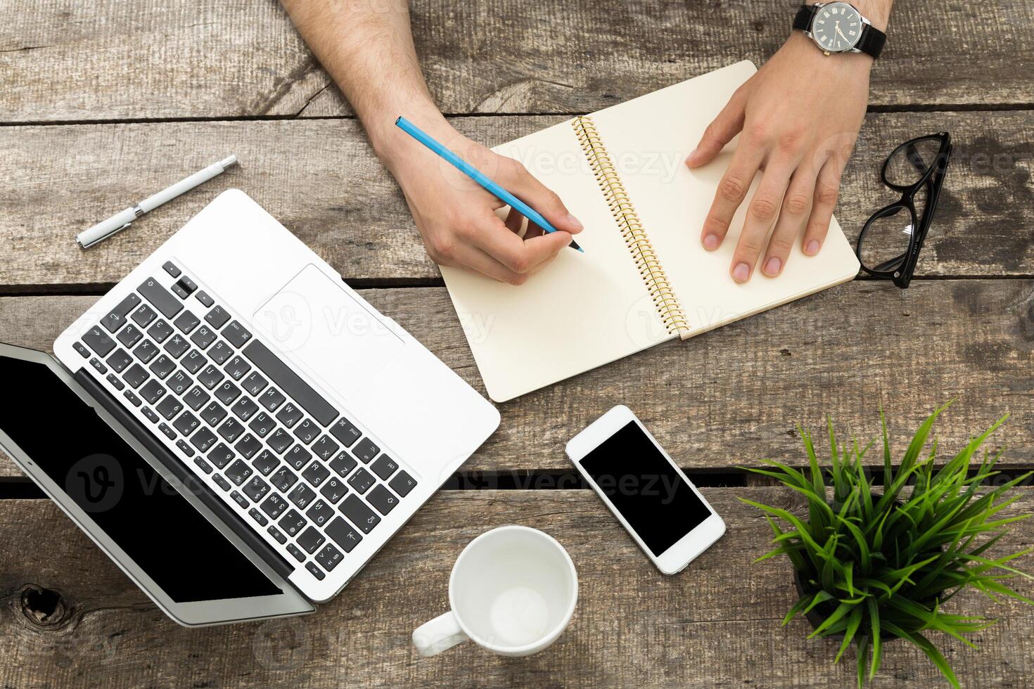 Creative workspace with a laptop, notepad, and smartphone on a rustic wooden table during a sunny afternoon photo