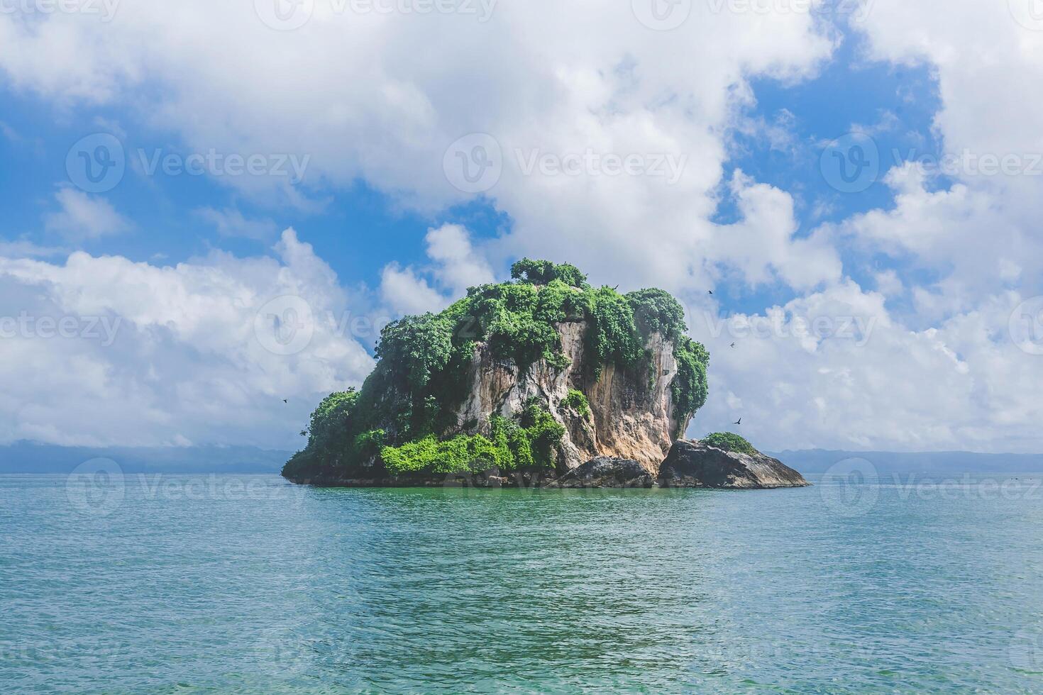 Island with lush greenery under a bright blue sky and soft clouds in a serene ocean setting photo