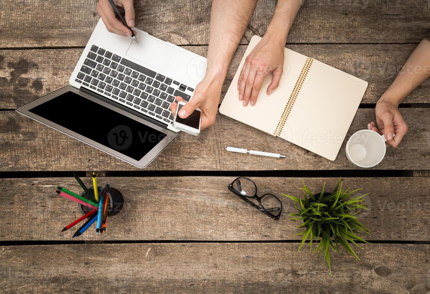 Collaborative work session at a rustic wooden desk with laptop, notebook, and coffee photo