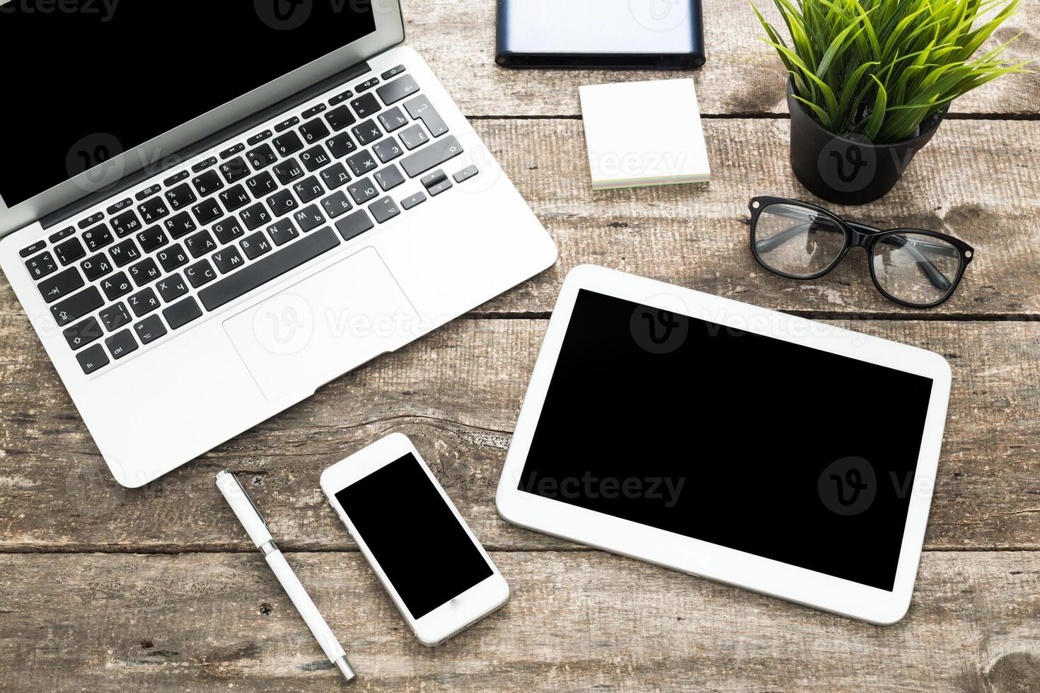 Workspace setup with laptop, tablet, smartphone, and green plant on wooden table in a bright environment photo