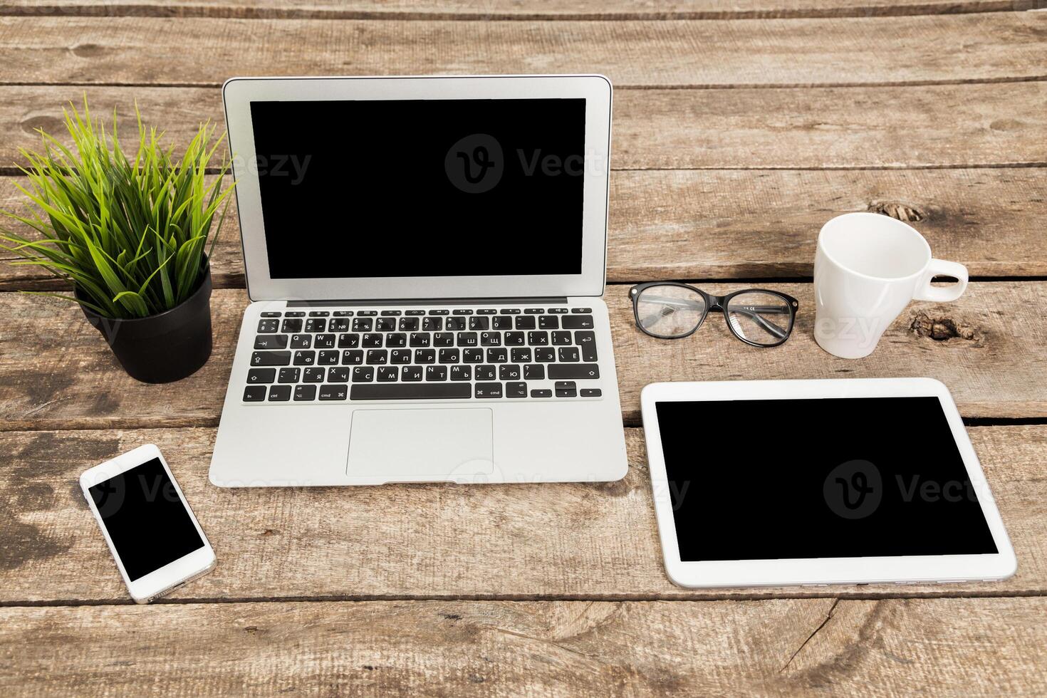 Workspace setup with laptop, tablet, smartphone, and coffee cup on wooden table during bright daylight photo