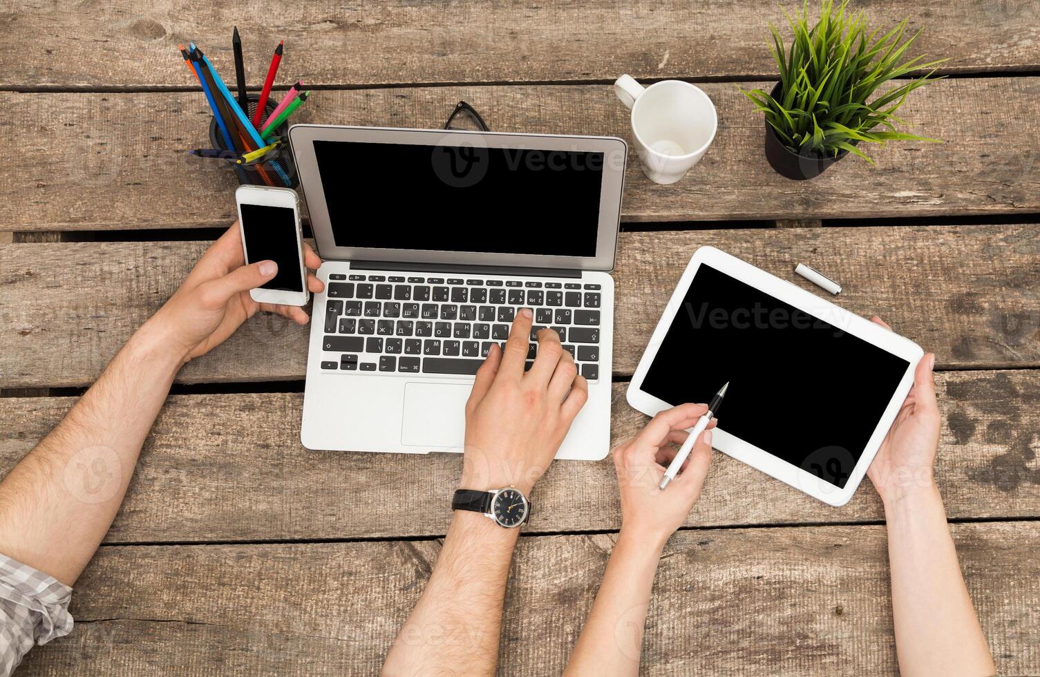 People engaged in technology multitasking at a rustic wooden table during work hours photo