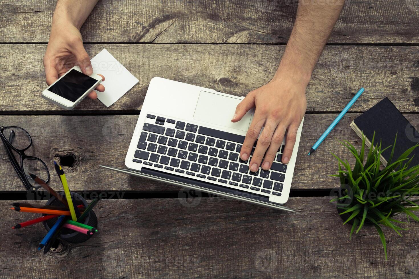 Working on a laptop while using a smartphone in a modern workspace with stationery and plants photo