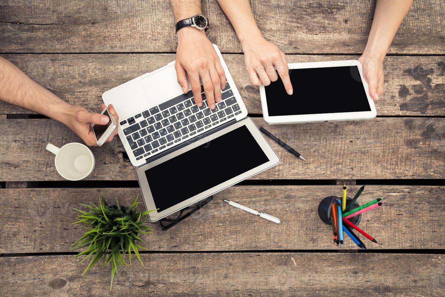 Collaborative workspace on wooden table with digital devices, cups, and stationery during a productive session photo