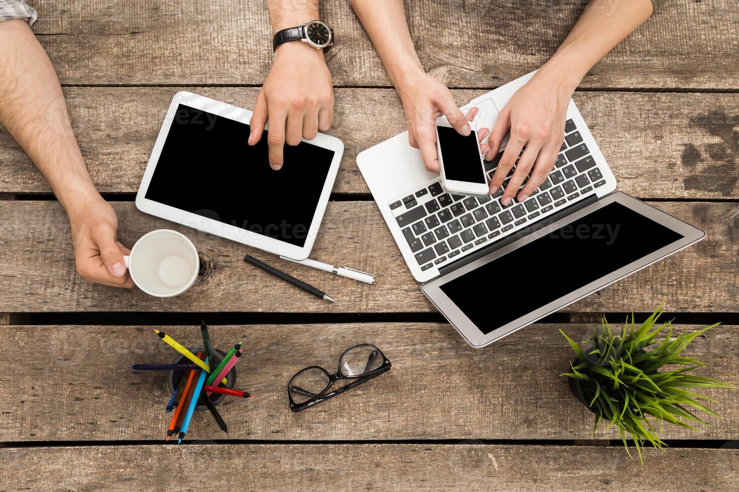 Collaborative workspace with technology and drinks at a wooden table during daytime hours photo