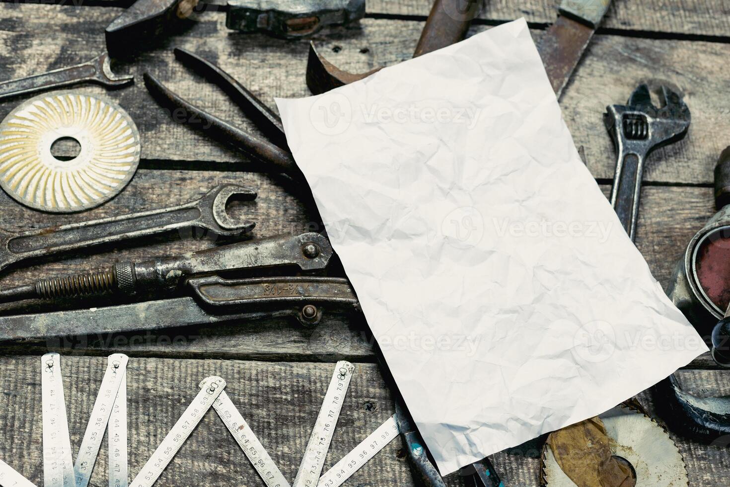 Various vintage tools scattered on a wooden surface with a blank piece of paper ready for notes or sketches photo