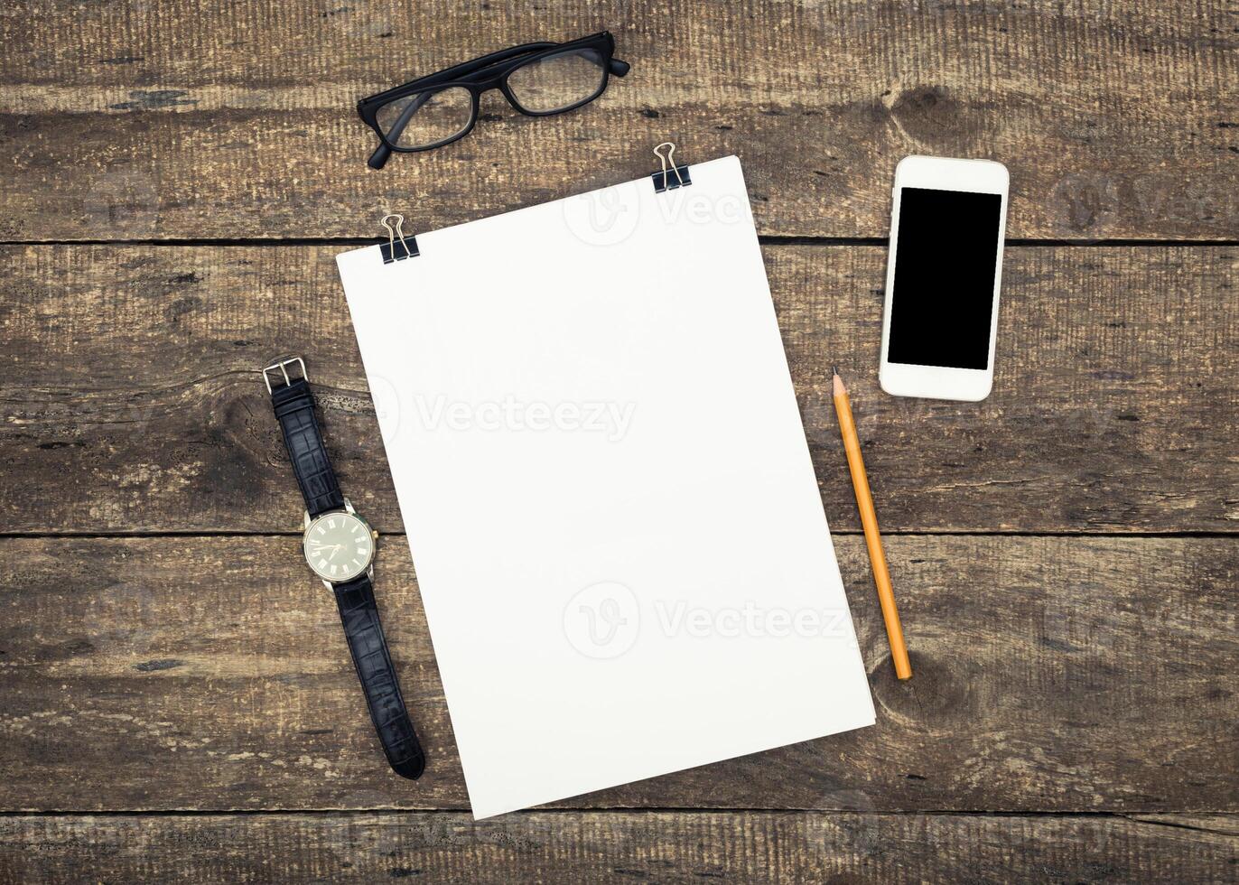 Workspace setup with blank paper, glasses, watch, pencil, and smartphone on rustic wooden table photo