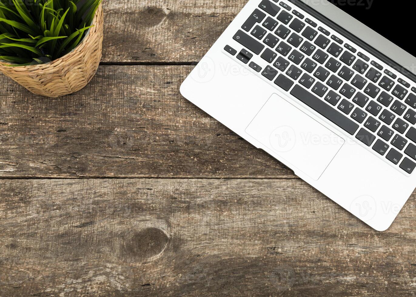 Laptop on rustic wooden table with potted plant in a cozy workspace during daylight hours photo
