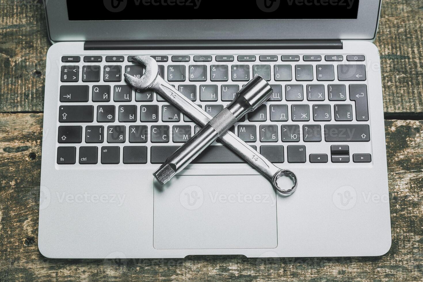 Crossed wrenches placed on a laptop keyboard against a rustic wooden background symbolizing technology and repair photo