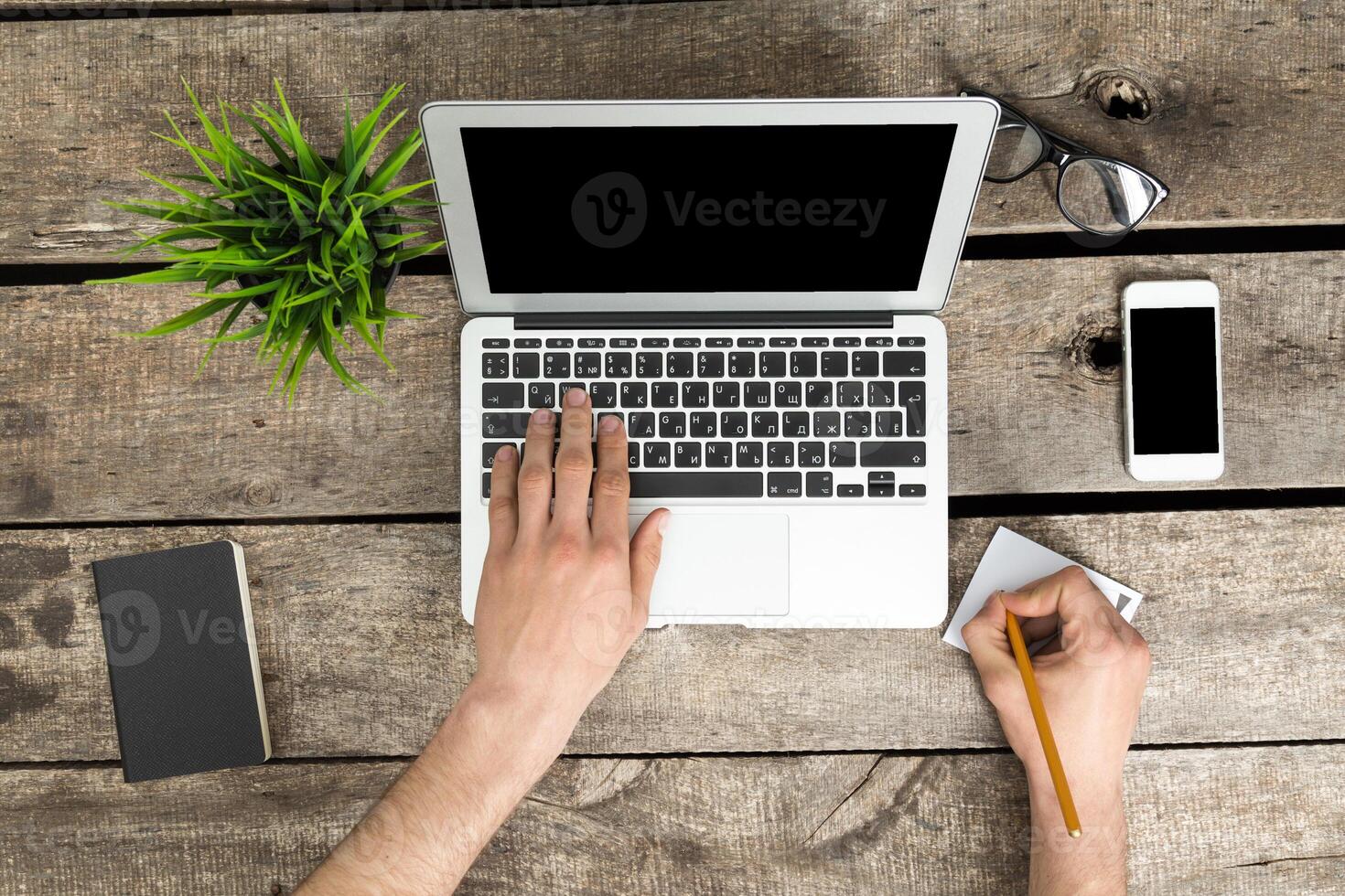 Writing notes while working on a laptop at a wooden desk with office supplies during the day photo