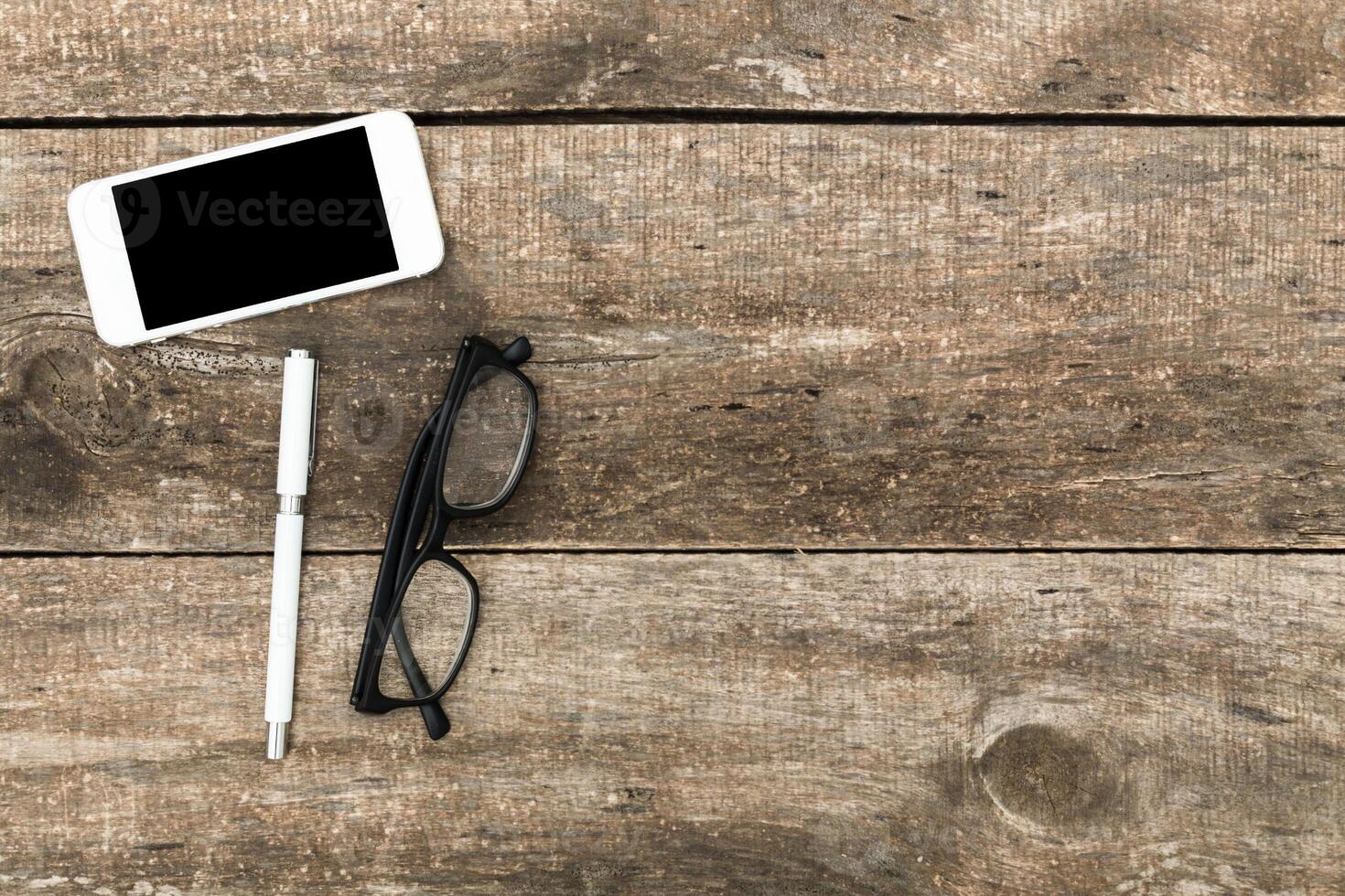 Workspace setup with smartphone, pen, and glasses on wooden table during the afternoon photo