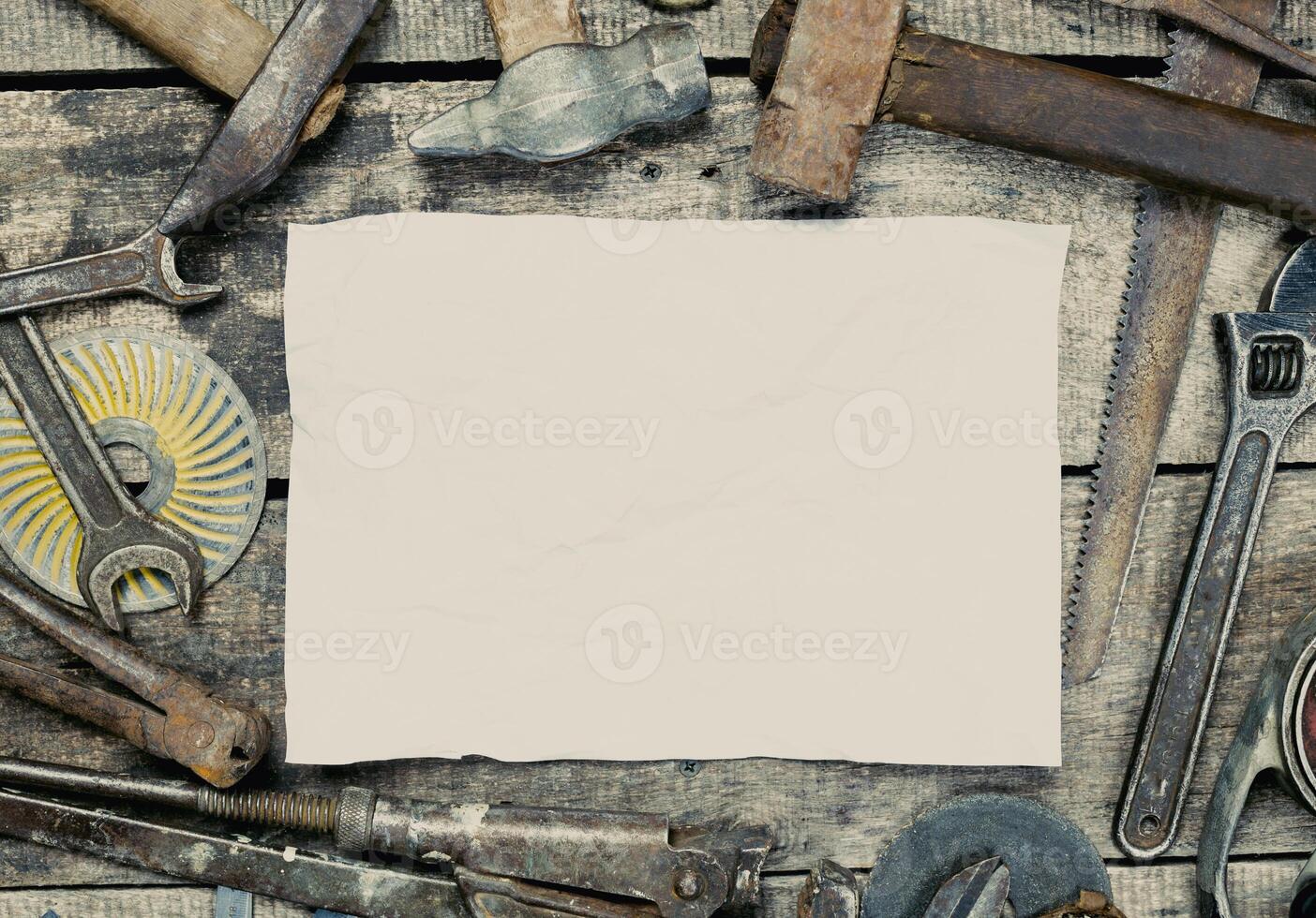 Various hand tools arranged around a blank sheet of paper on a wooden table ready for a project photo