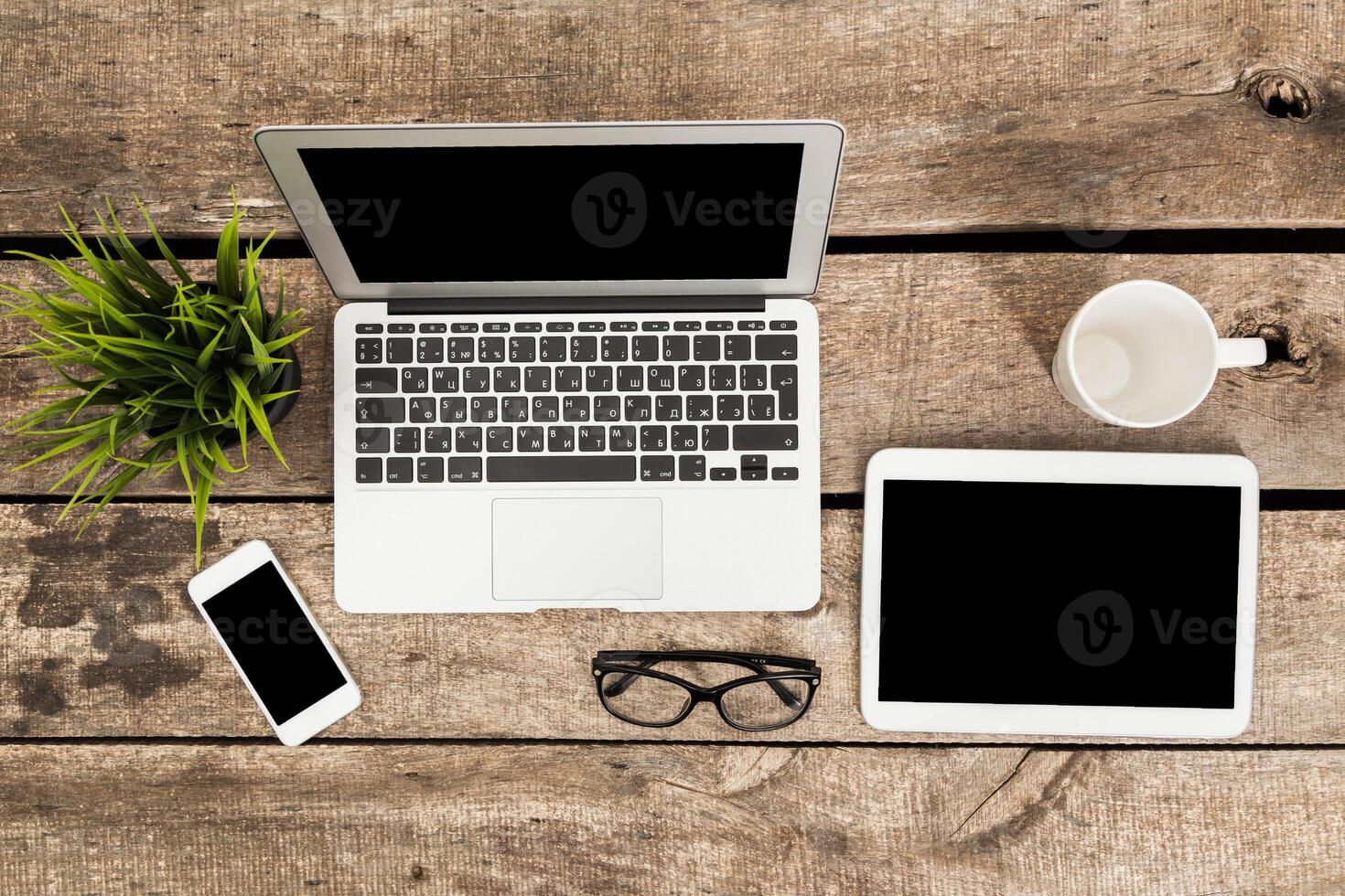 Workspace setup with laptop, tablet, smartphone, and coffee cup on a wooden table during daylight hours photo