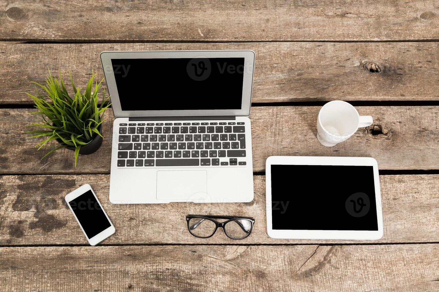 Workspace with laptop, tablet, smartphone, and coffee cup arranged on rustic wooden table during daytime photo
