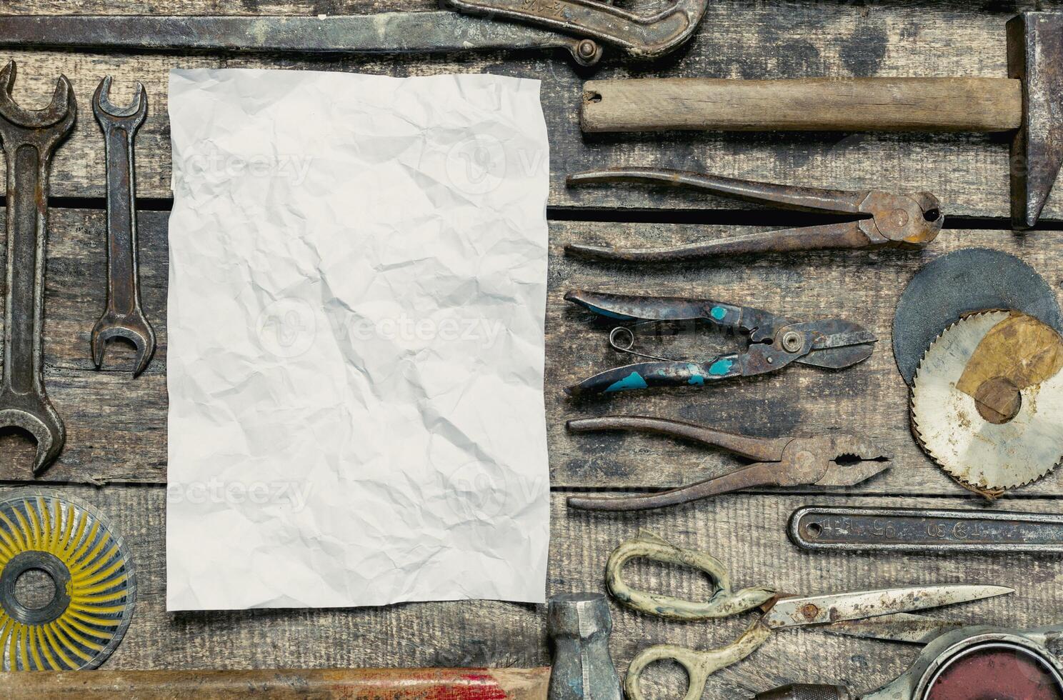 Crafting tools arranged around a blank sheet on a weathered wooden table in a workshop setting photo