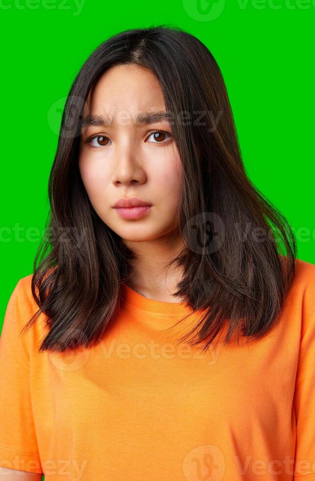 Young woman with long dark hair in orange shirt expresses curiosity against a bright green background photo