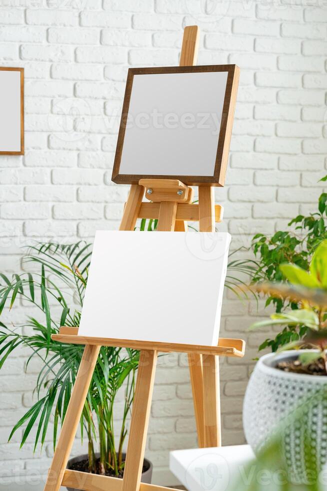 Blank canvas on wooden easel surrounded by indoor plants in a bright, minimalist studio space photo