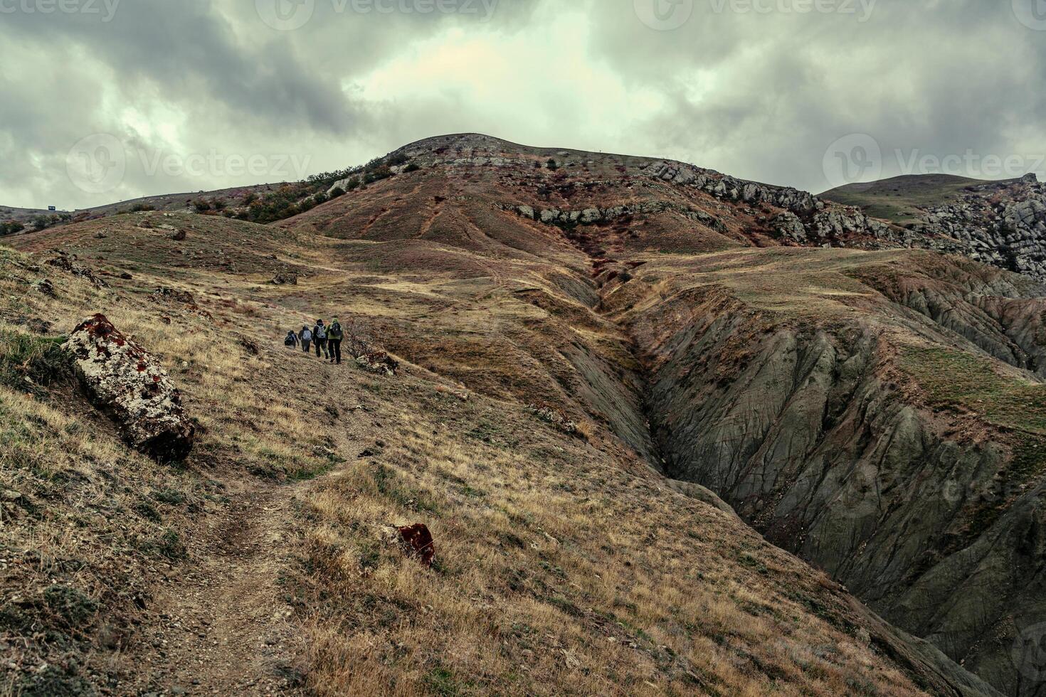 Hikers travel across a rugged mountain landscape under a cloudy sky in a remote area during early morning hours photo