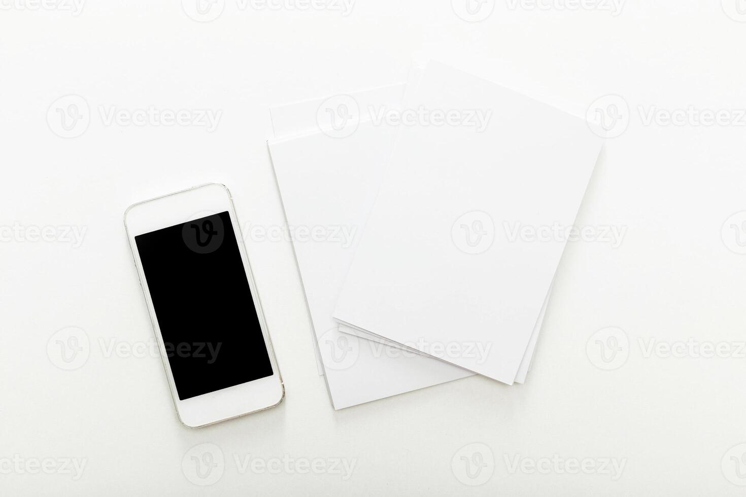 Smartphone and blank sheets resting on a white table, ideal setup for digital note-taking and brainstorming sessions photo