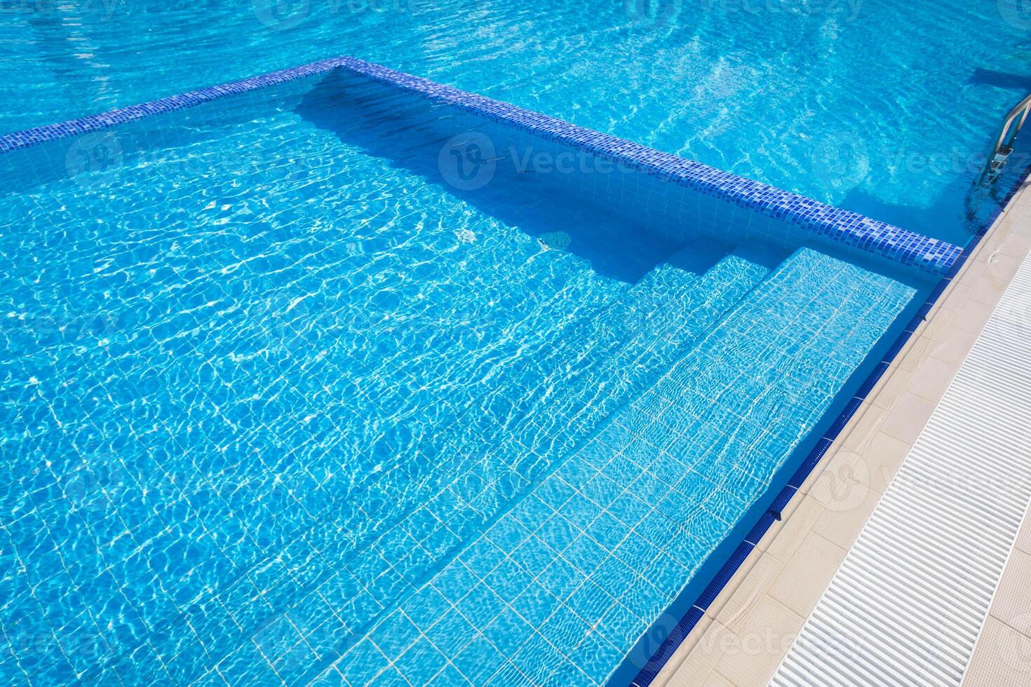 Bright blue swimming pool reflecting sunlight, showcasing inviting steps and clear water on a sunny day photo