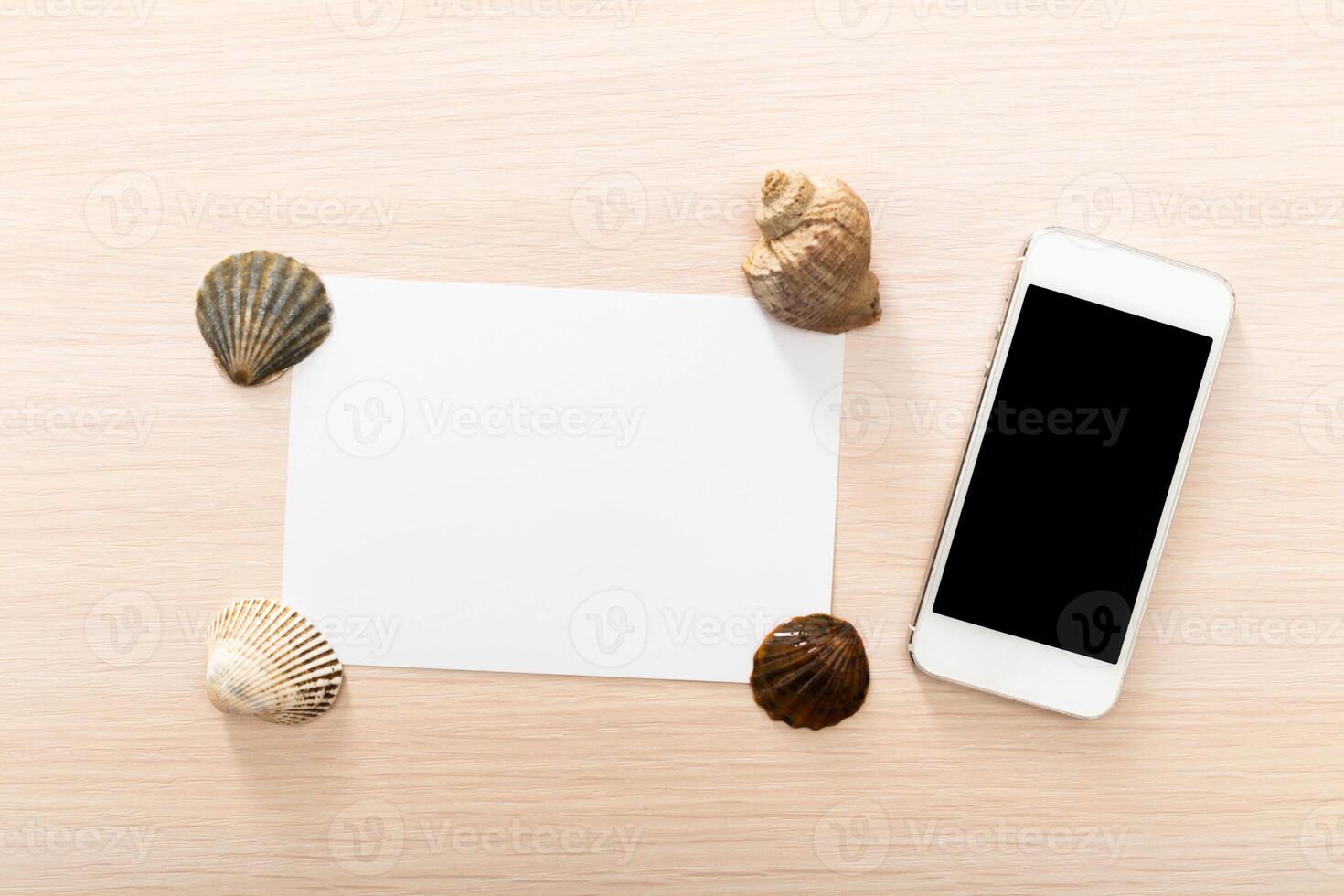 Blank card and smartphone surrounded by seashells on light wooden surface photo