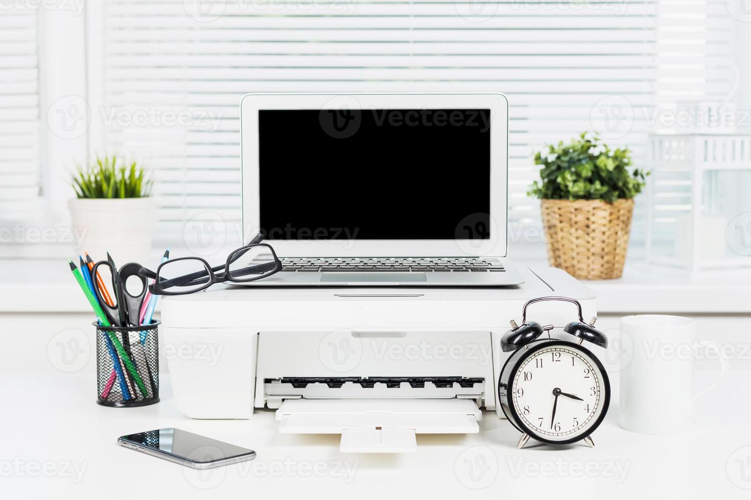 Desk setup with laptop, printer, and office supplies during daytime in a modern workspace photo