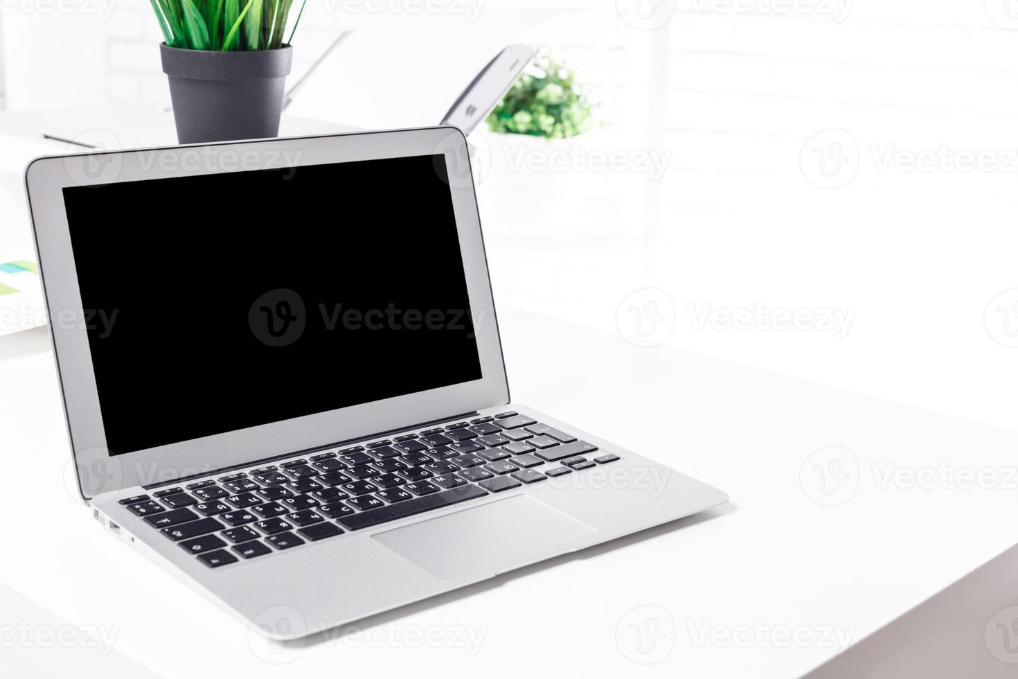 Modern workspace with empty laptop on desk and green potted plant in bright and airy environment photo