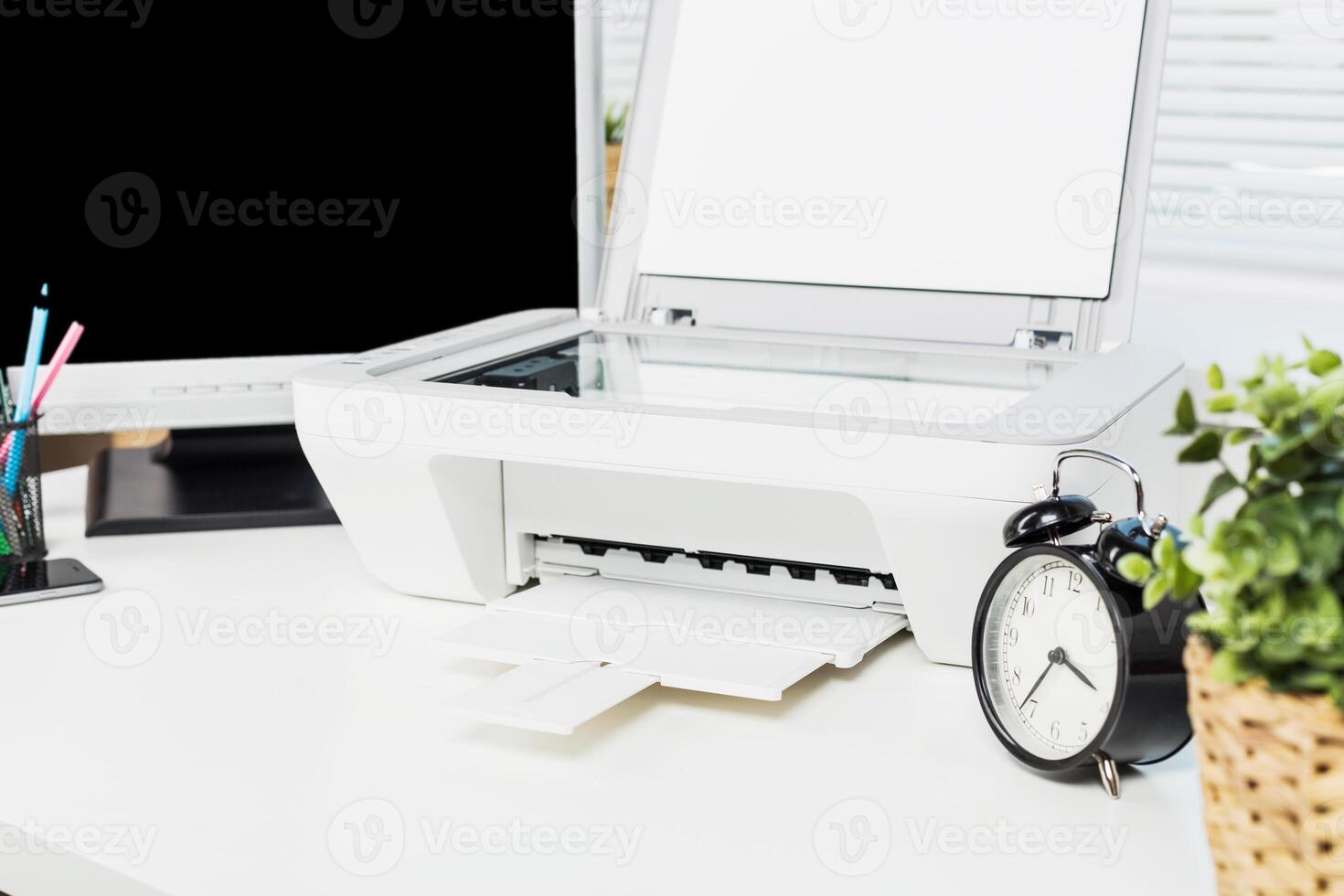 Desk setup features a printer, clock, and plants in a bright workspace promoting productivity and organization photo