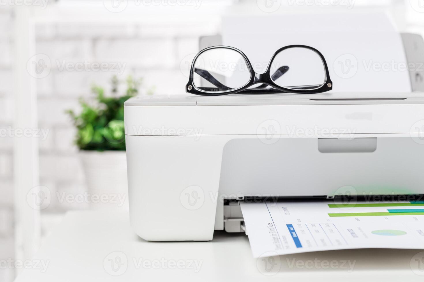 Printer with glasses and documents on a desk in a bright office environment during daytime photo