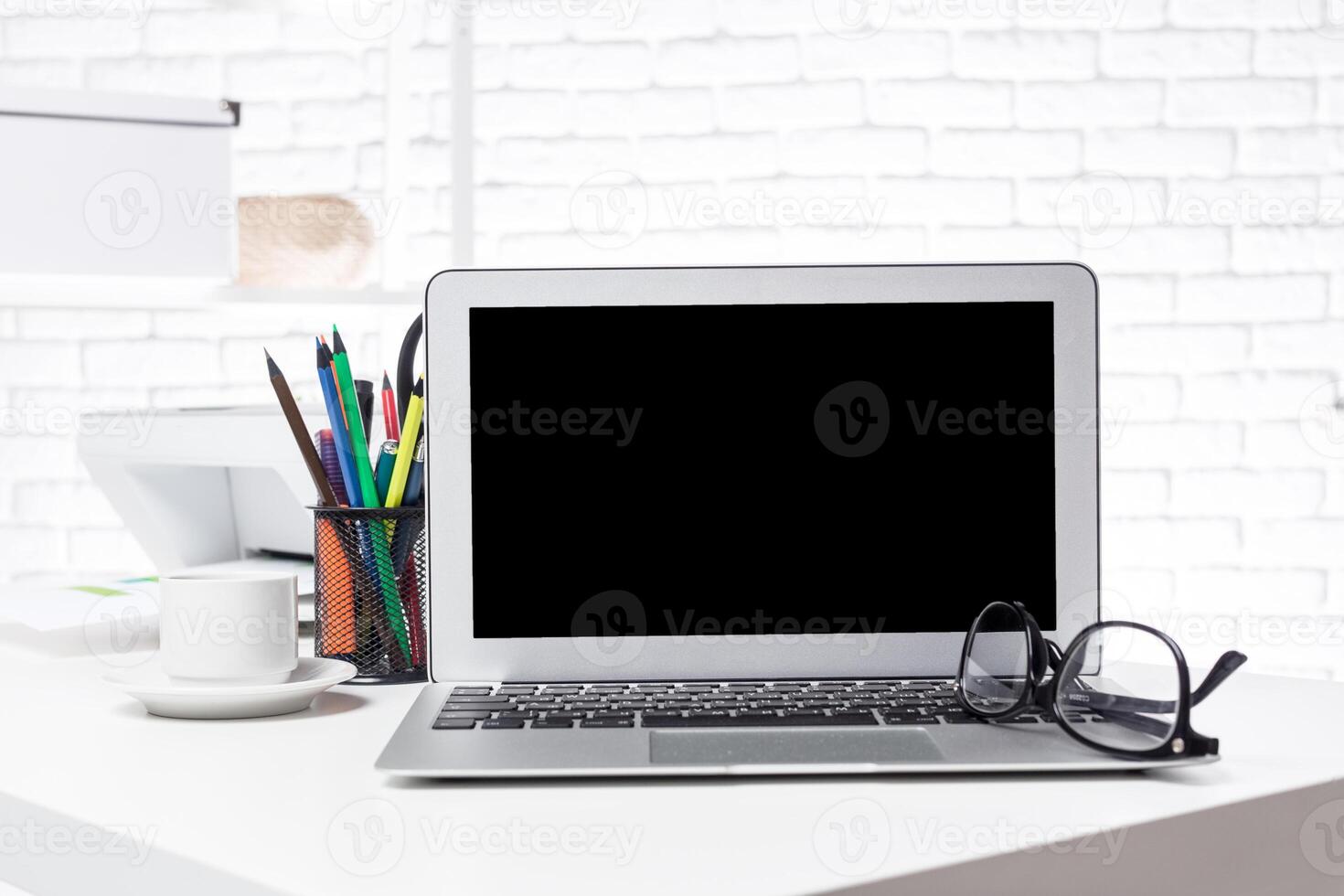 Modern workspace with laptop, glasses, and stationery in a bright office setting photo