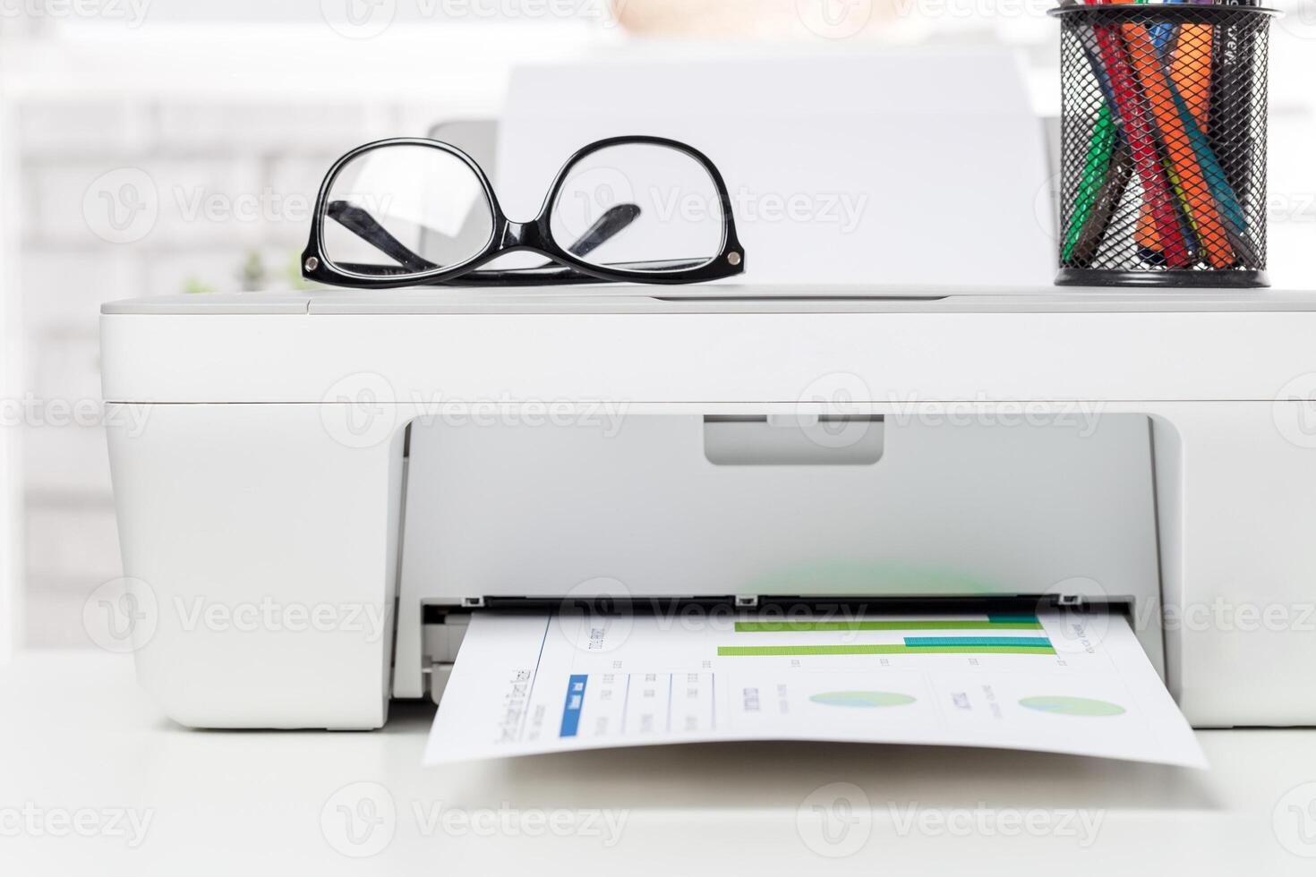 Printer producing financial report on desk with glasses and pen holder during daylight photo