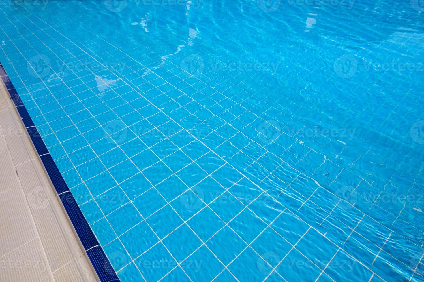 Clear blue swimming pool with tiled edges reflecting sunlight during a warm afternoon photo