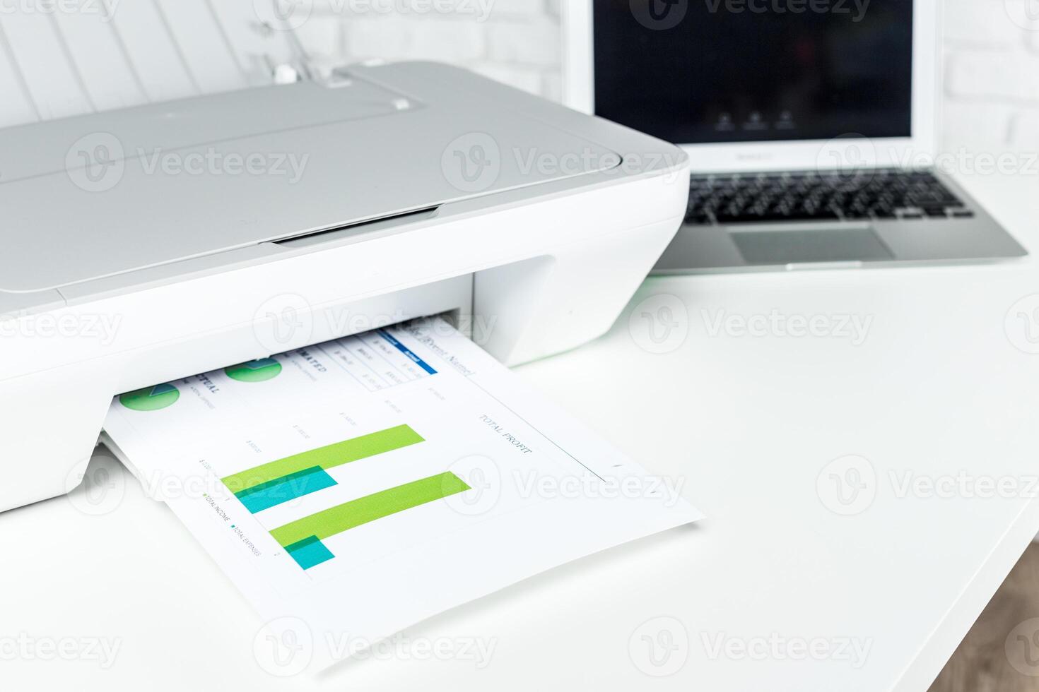 Printer producing document with color graphics beside a laptop on a modern workspace photo