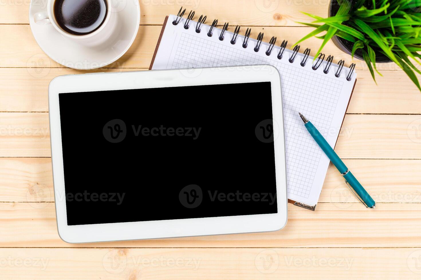 Workspace setup with tablet, coffee, notebook, and plant on wooden table photo