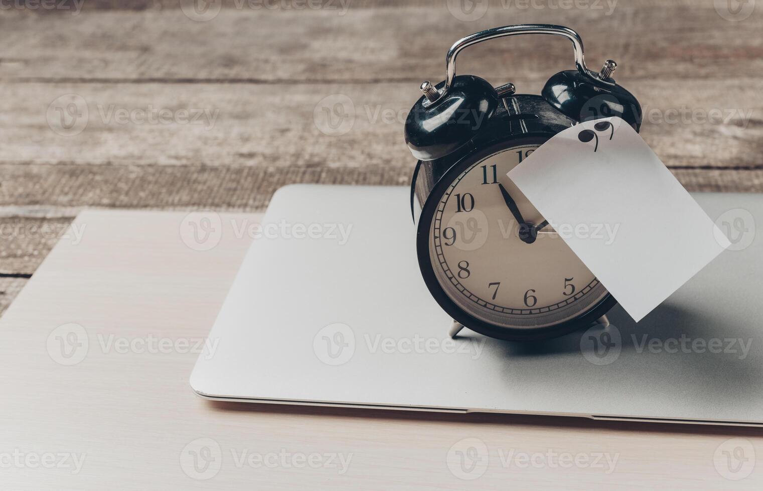 Classic black alarm clock on laptop with price tag resting on wooden table in cozy workspace setting photo