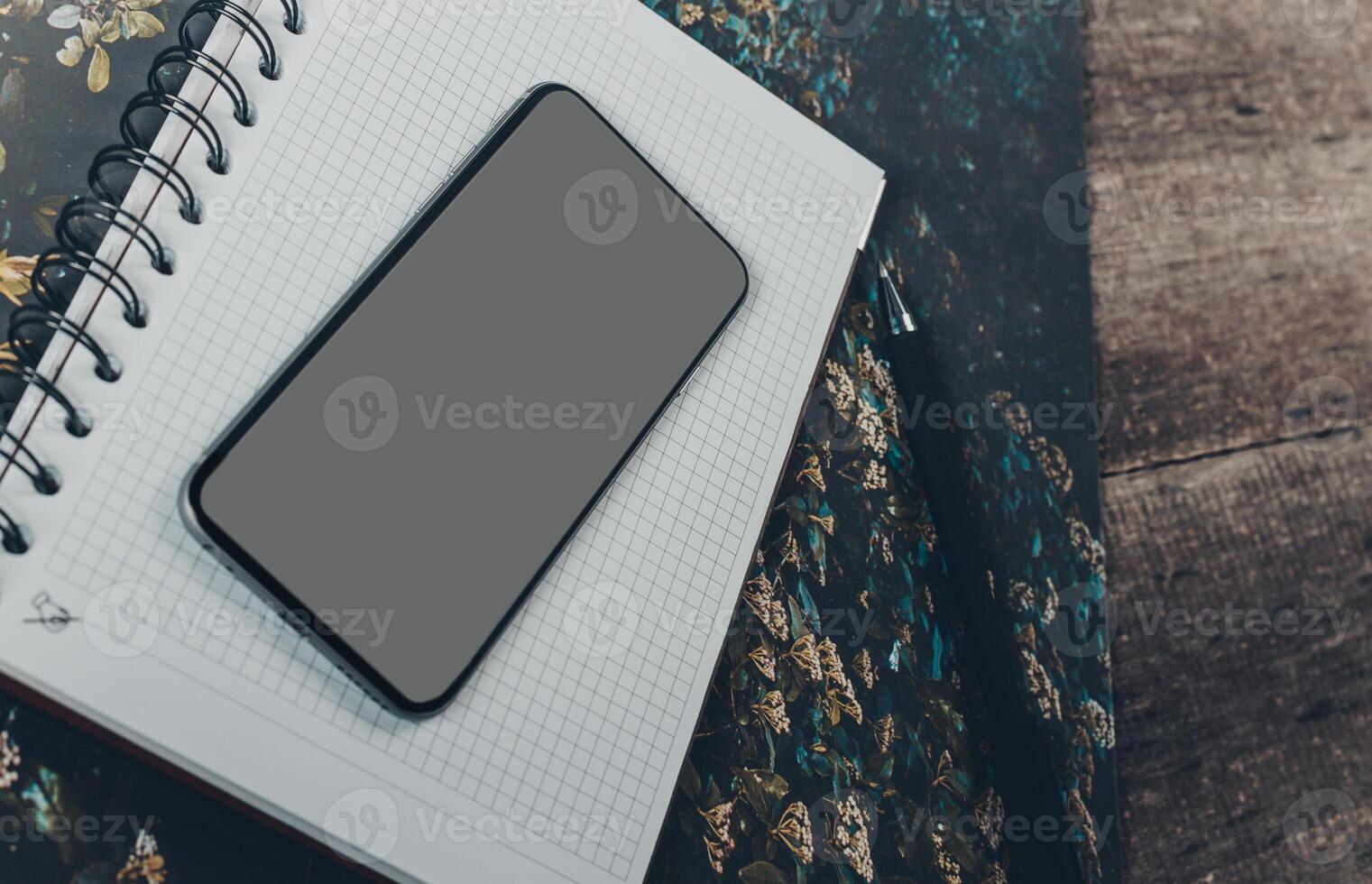 Smartphone resting on a blank notepad on a textured wooden surface during a quiet afternoon photo