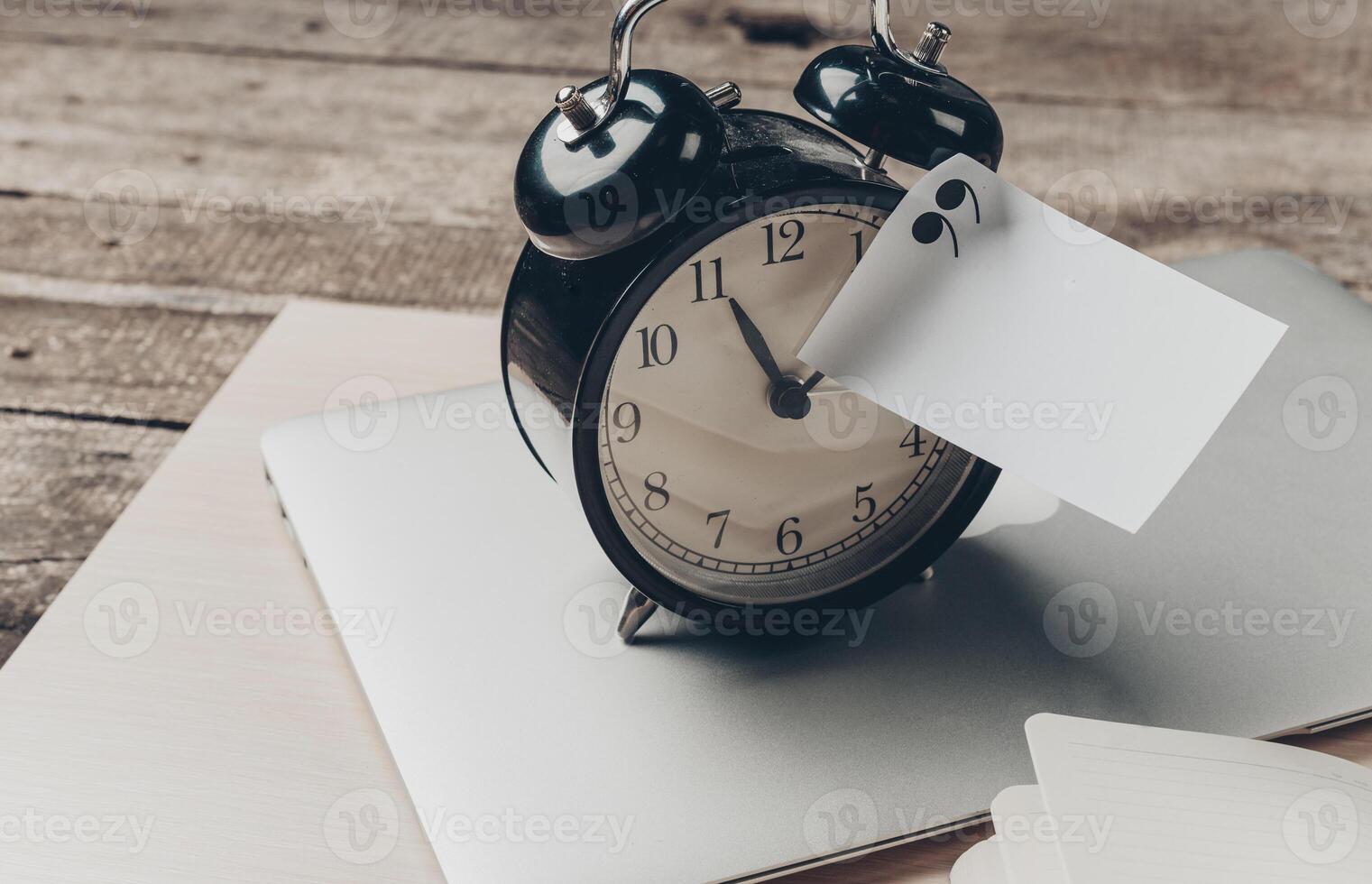 Clock on a laptop with a note attached is a reminder for tasks at a workspace photo