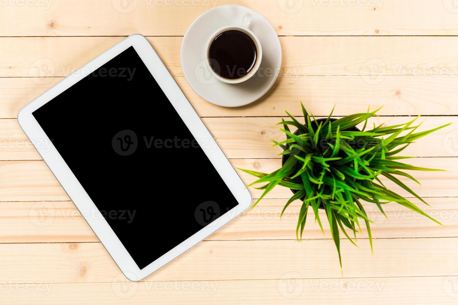 Coffee cup and tablet on a wooden table with a potted plant in a cozy setting during the day photo