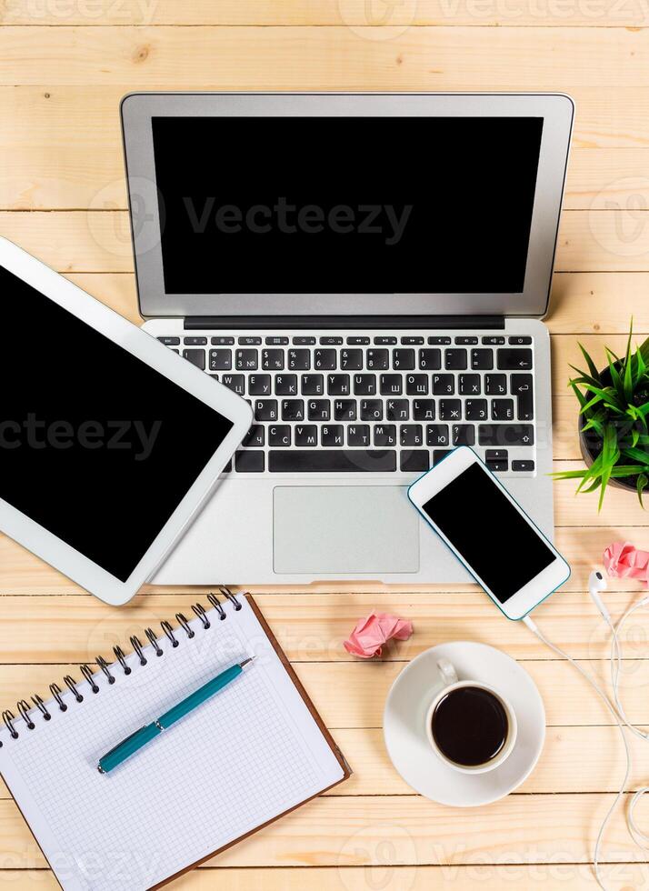 Workspace setup featuring laptop, tablet, smartphone, and coffee cup on wooden desk at early morning photo
