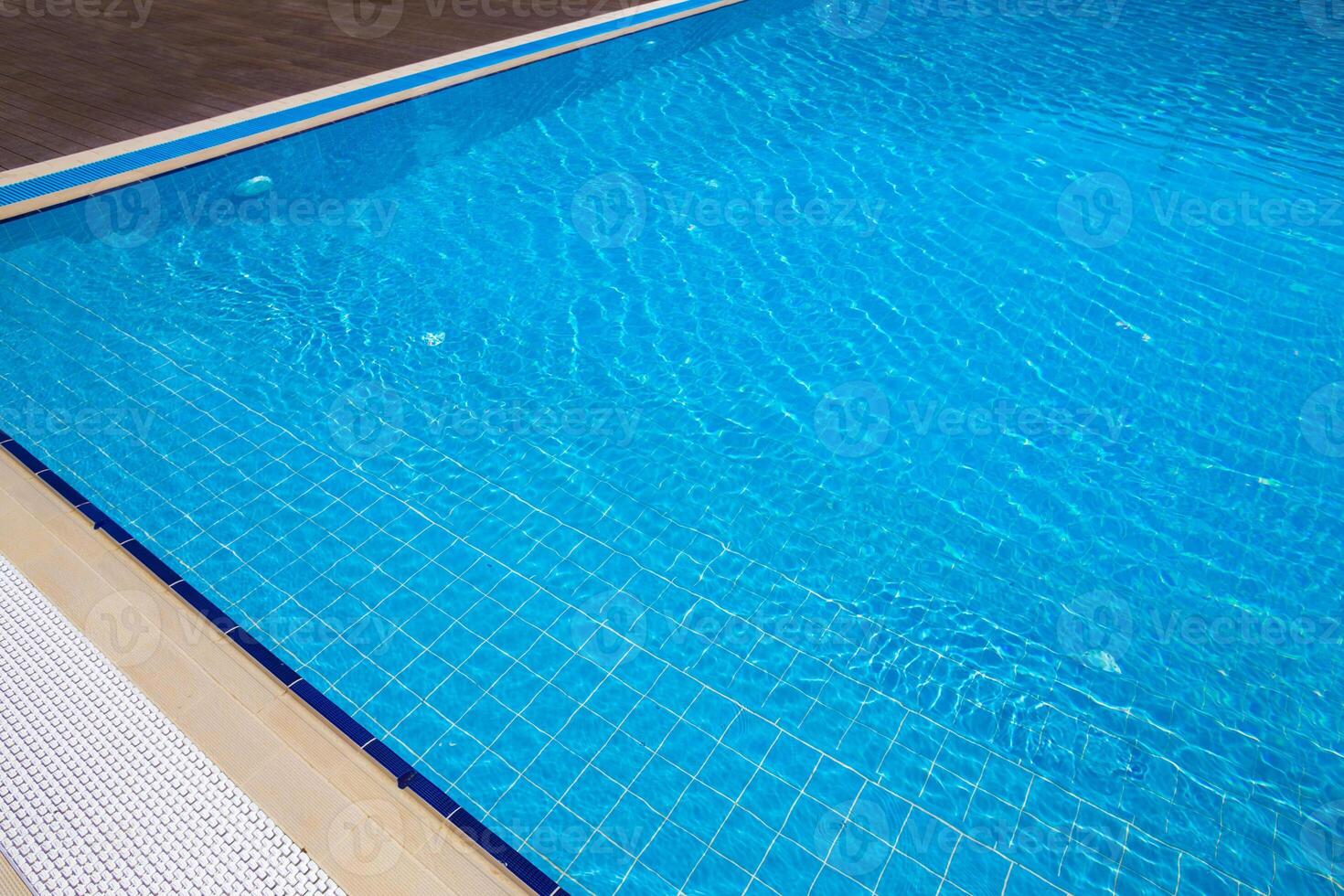Sparkling blue water glistens under sunlight at a pristine swimming pool in a serene outdoor setting photo