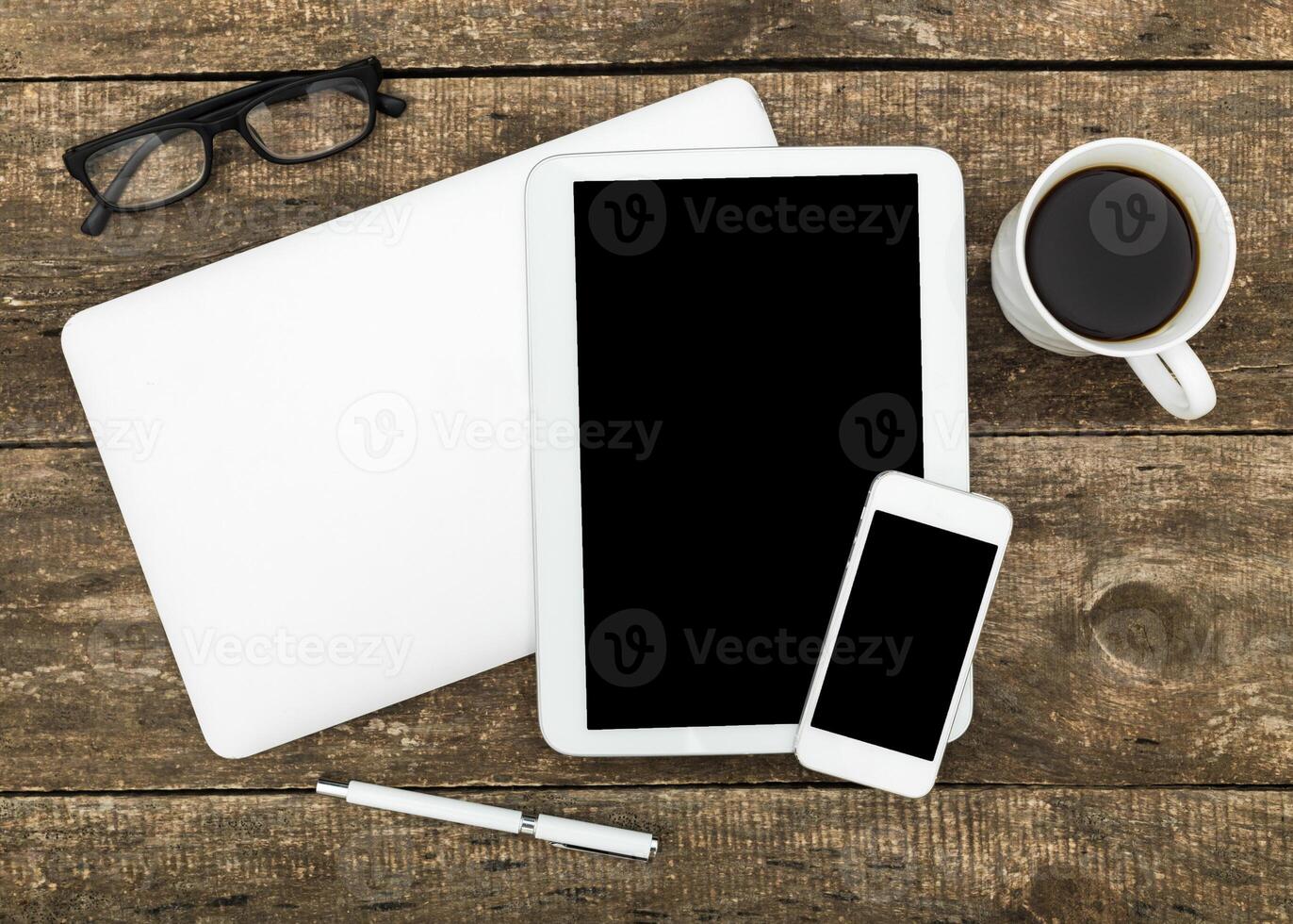 Workspace setup featuring gadgets, coffee, and stationery on wooden table photo