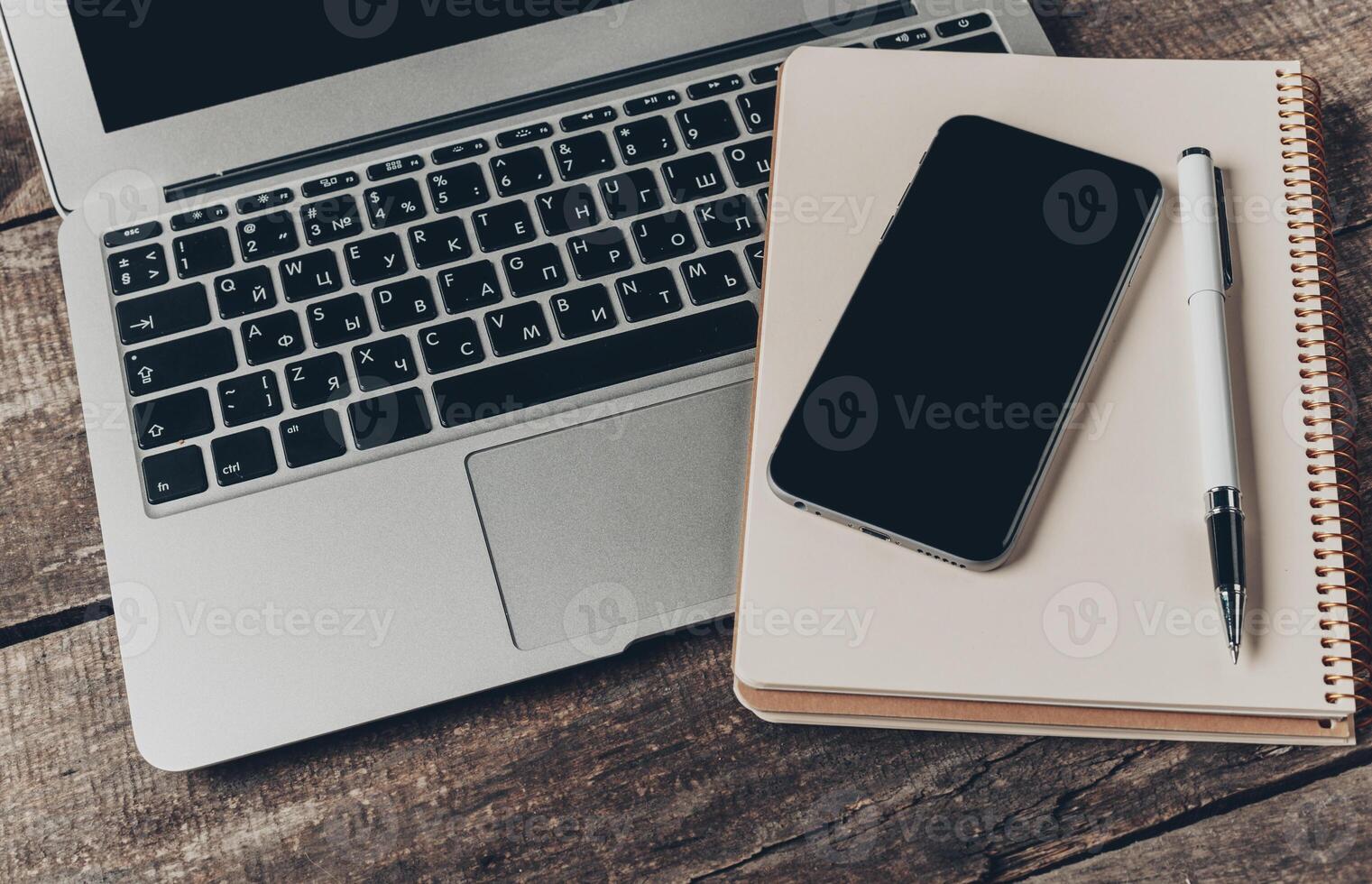 Workspace setup featuring a laptop, smartphone, and notebook on a rustic wooden table photo