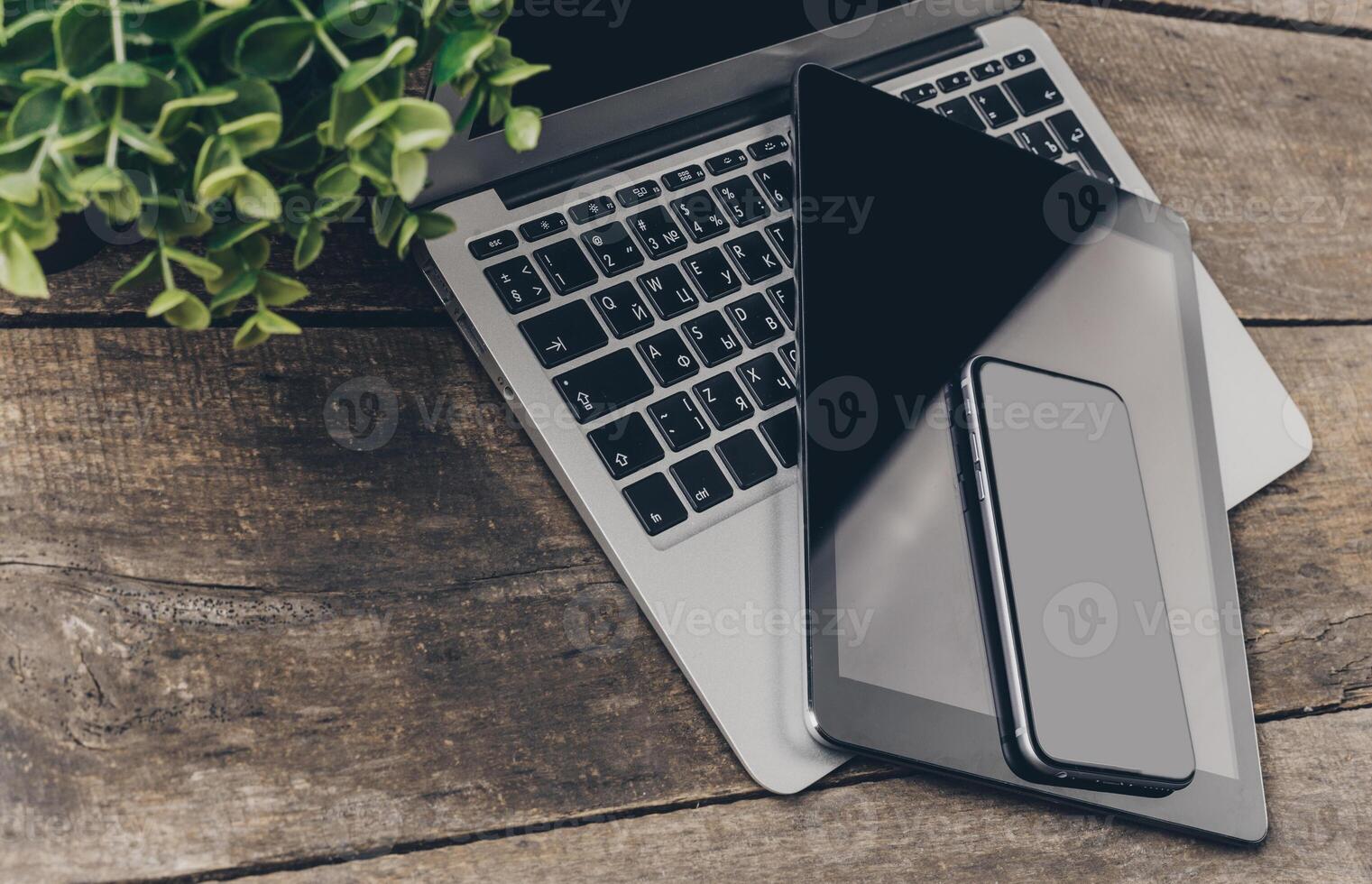 Digital workspace featuring a laptop, tablet, and smartphone on a rustic wooden surface with greenery in view photo