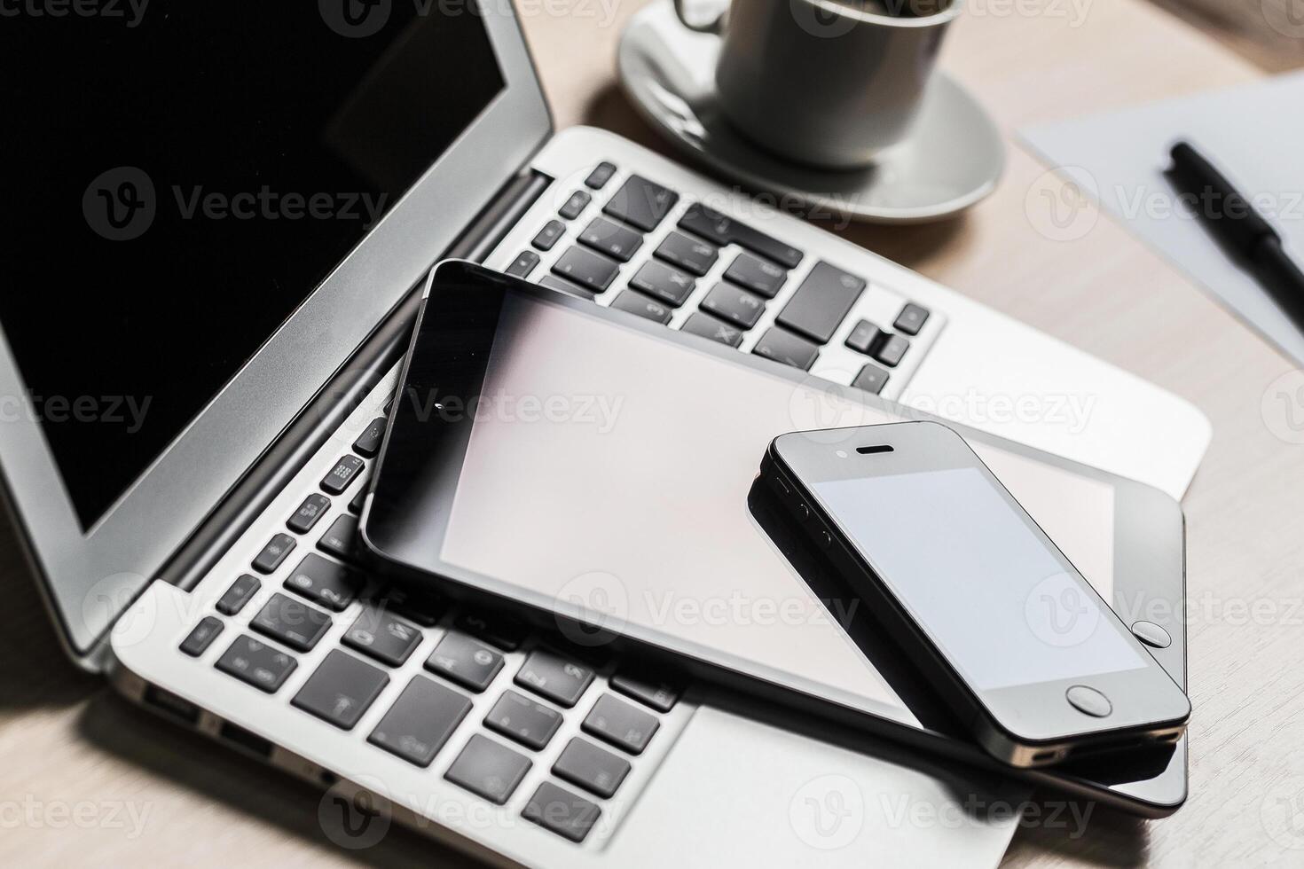Multiple electronic devices including a laptop, tablet, and smartphone are organized on a desk with a coffee cup nearby photo