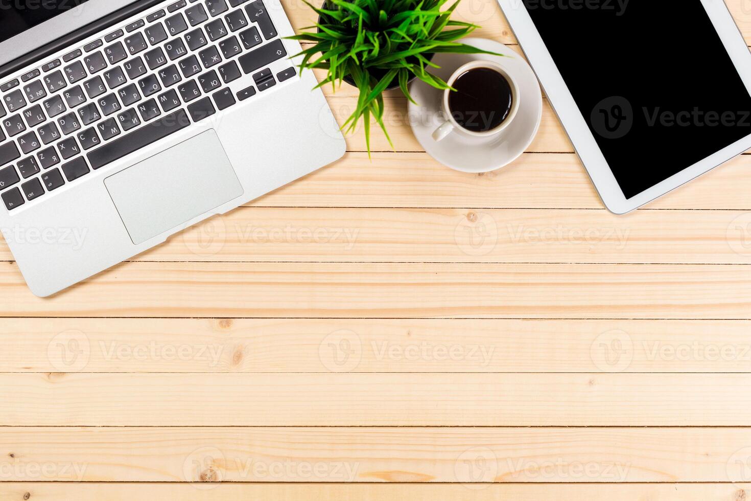 Workspace setup with laptop, tablet, coffee cup, and plant on wooden table in a modern environment photo