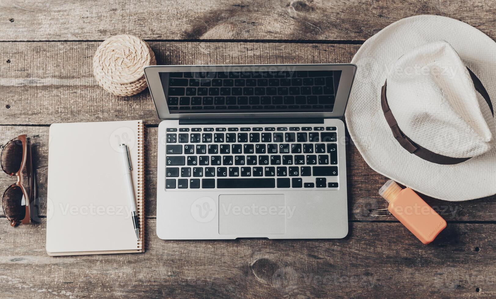 Relaxed workspace setup with a laptop, notebook, and summer accessories on a wooden table photo