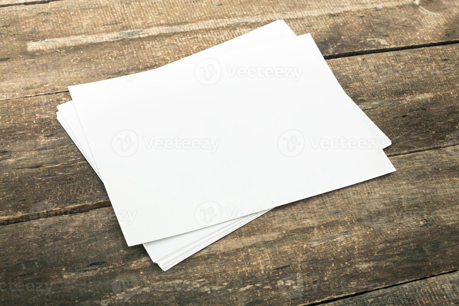 Blank sheets of paper stacked on a weathered wooden table at a creative workspace during daylight hours photo