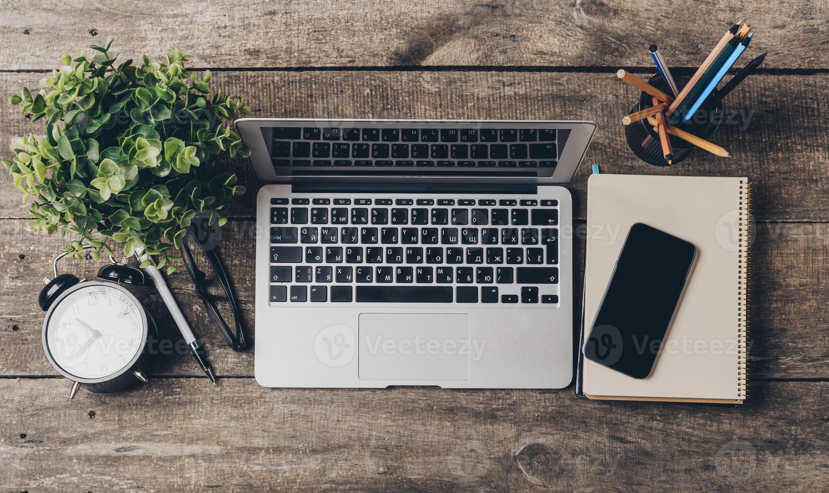 Modern workspace with laptop, clock, and stationery on wooden table during daylight photo