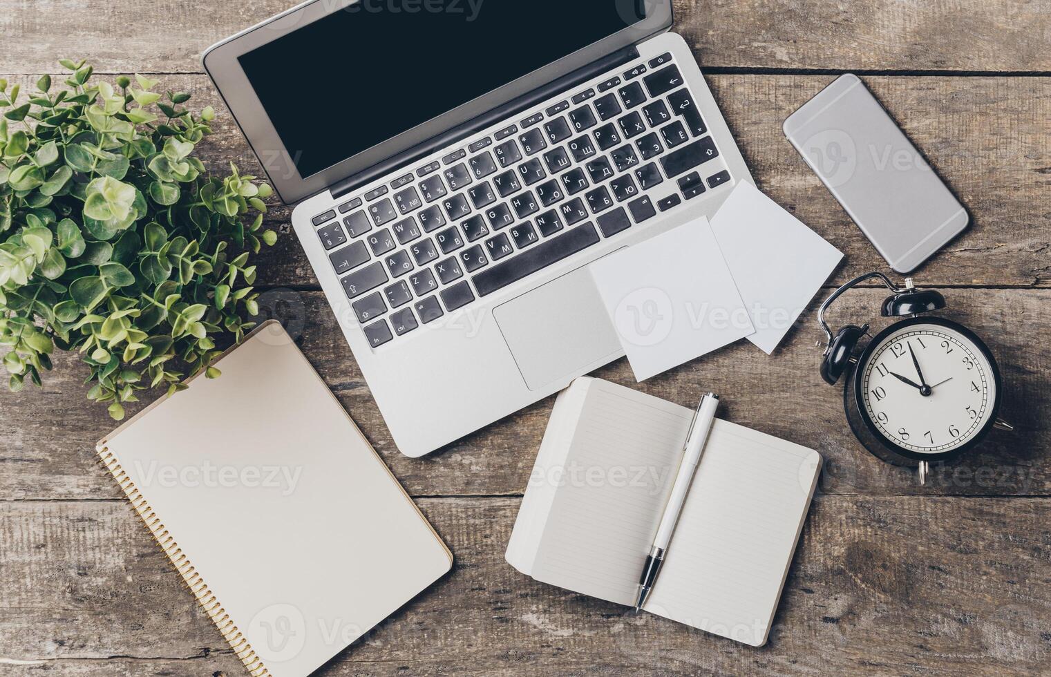 Workstation setup with laptop, clock, and notepads on wooden desk in a cozy and organized environment photo