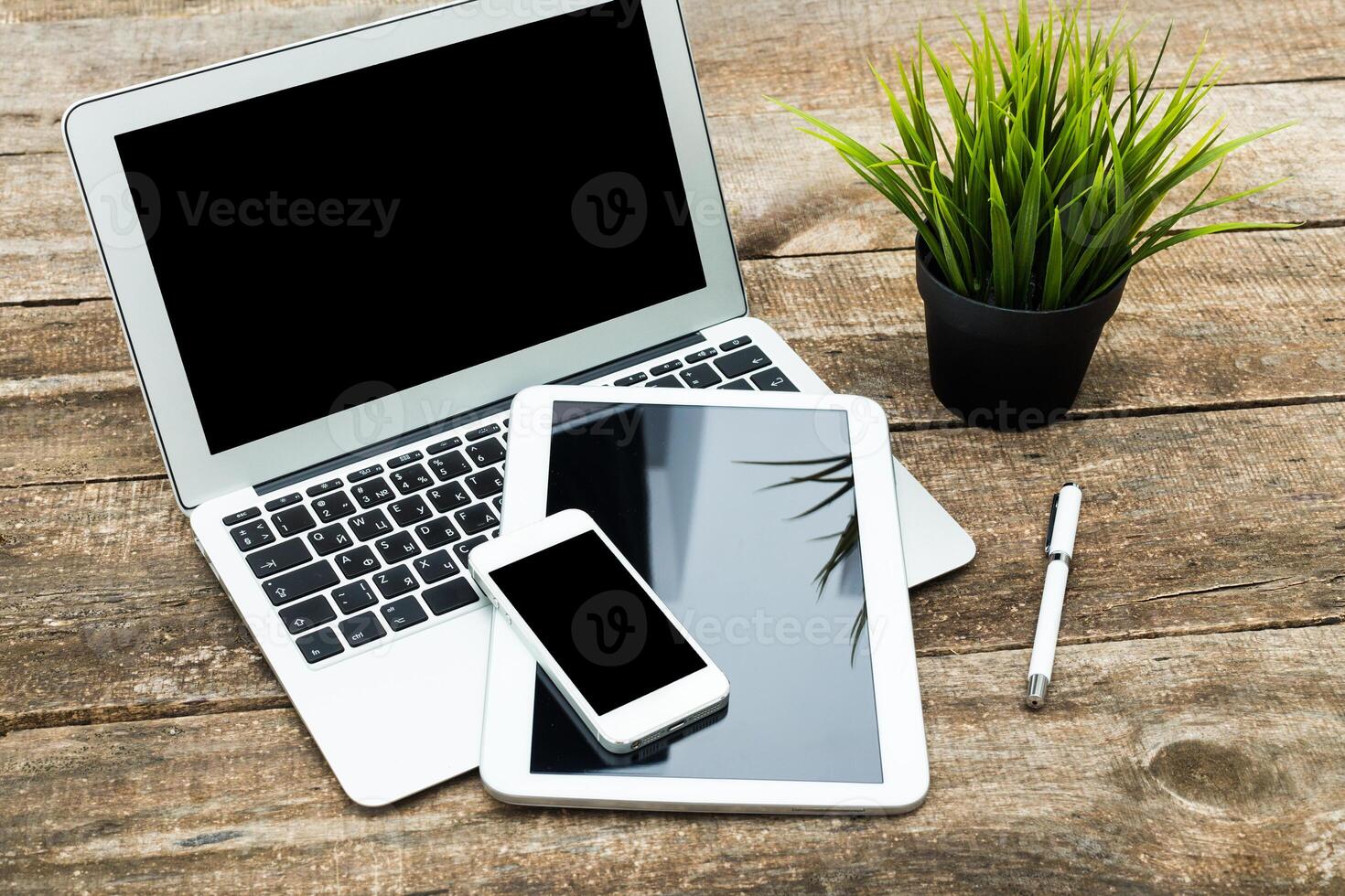 Workspace setup featuring a laptop, tablet, smartphone, and plants on a wooden table during daytime photo